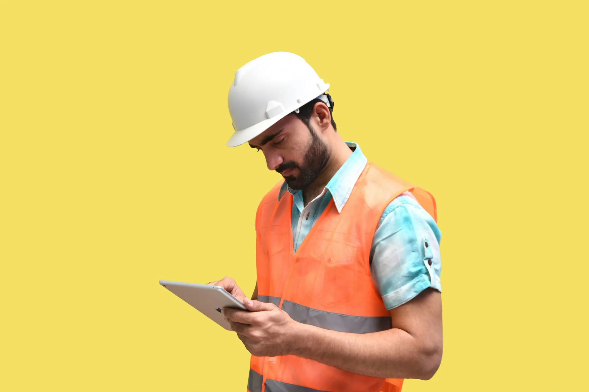 Electrician in a hard hat and safety vest reviewing plans on a tablet