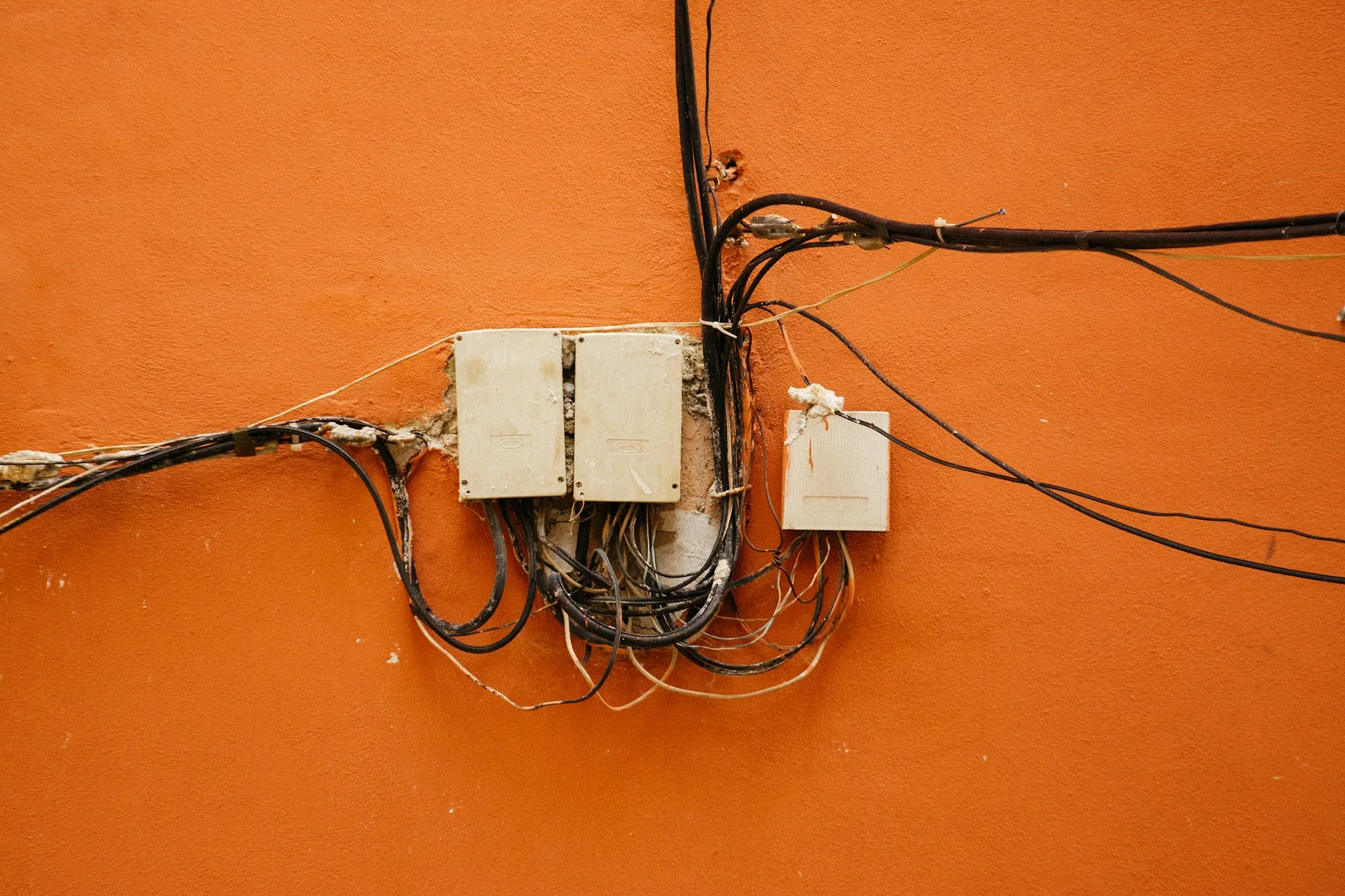 Old wiring and junction boxes mounted on an orange wall